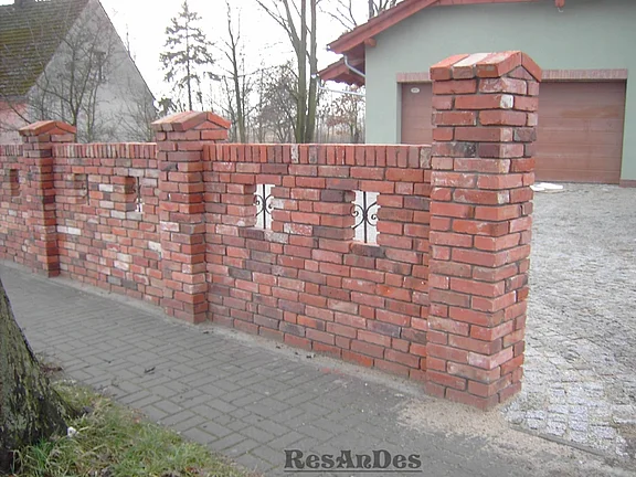 Massive Grundstückmauer aus alten Ziegelsteinen mit Säulen und dekorativen Fenstern aus Gusseisen