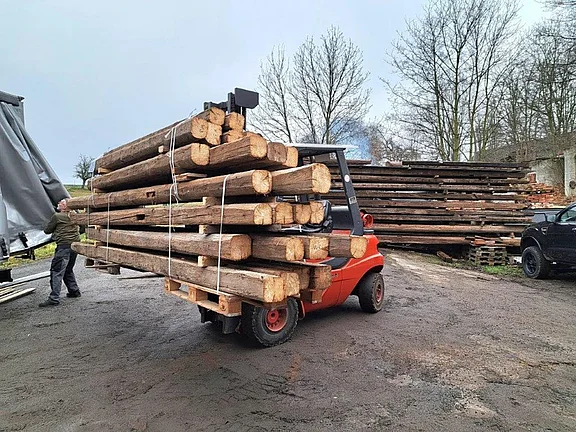 Stapler transportiert alte Holzbalken und historisches Bauholz zur Lieferung